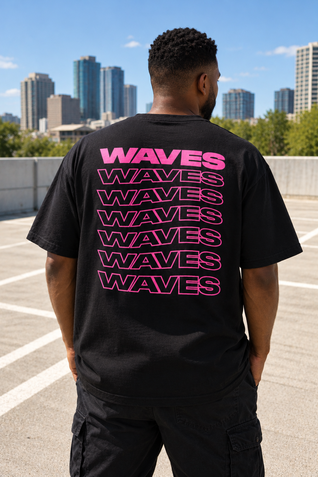T-shirt oversize WAVES noir vu de dos, avec typographie rose fuchsia répétée en cascade.